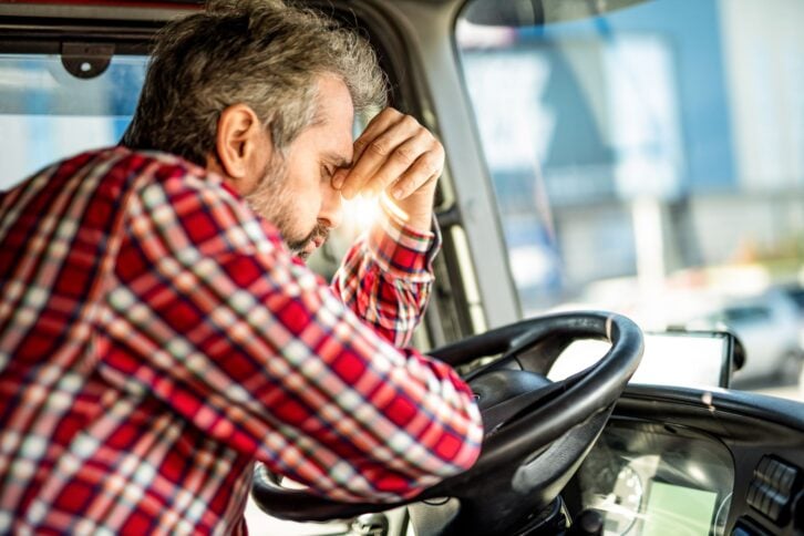 Distraught truck driver leaning on a steering wheel and having a headache.