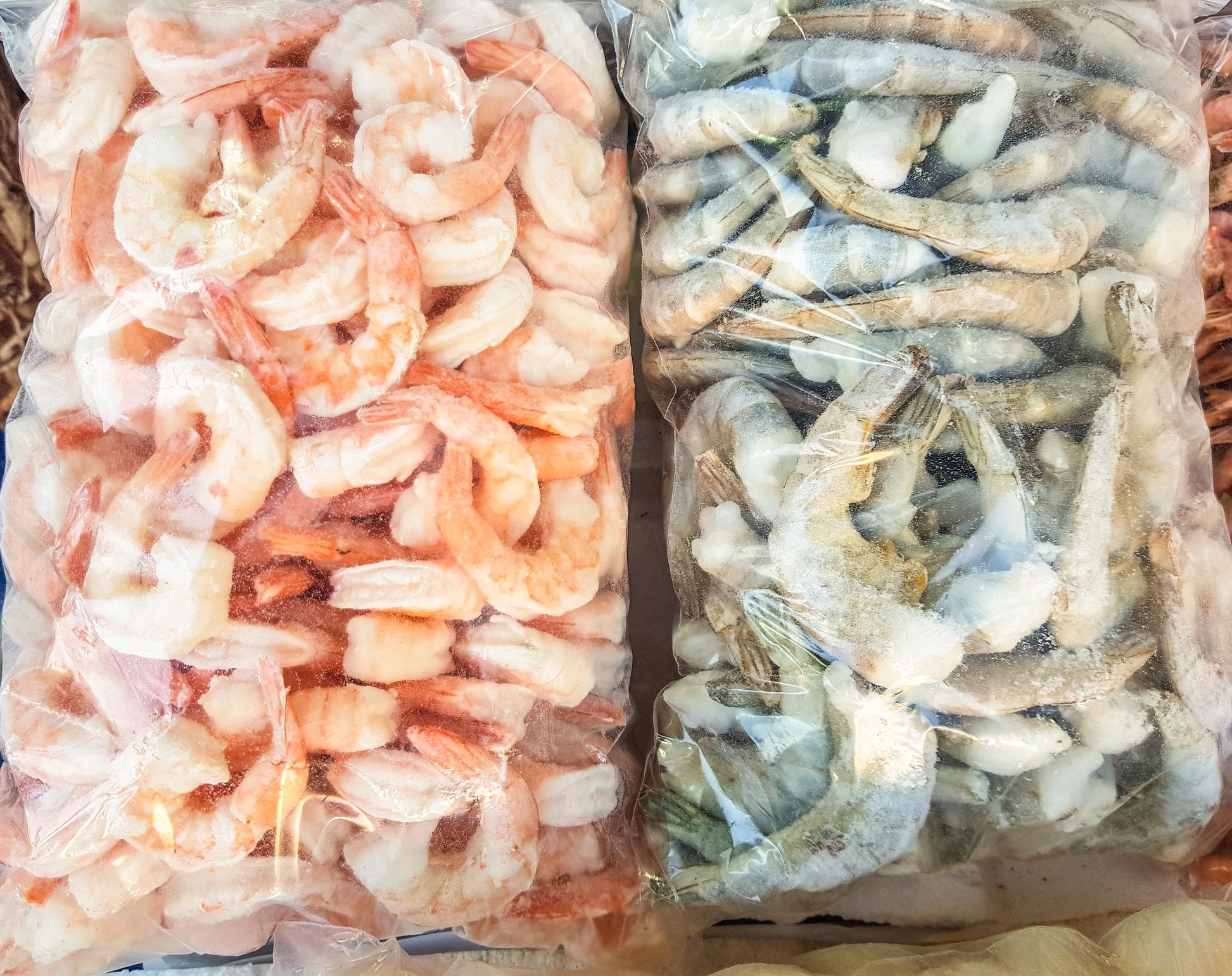 Two large plastic bags of frozen raw and cooked shrimp, on the counter of the fish market.