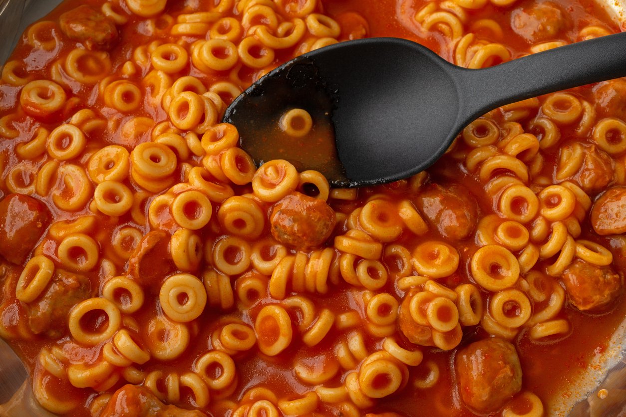 A close-up of spaghetti rings in tomato sauce with meatballs, being stirred by a black spoon.