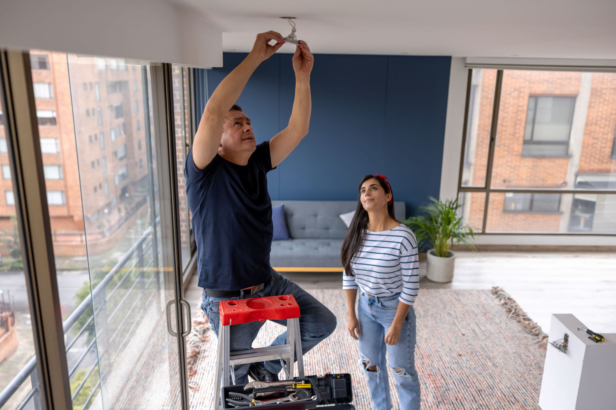 Latin American electrician fixing a light bulb at a womanâs house - domestic life concepts