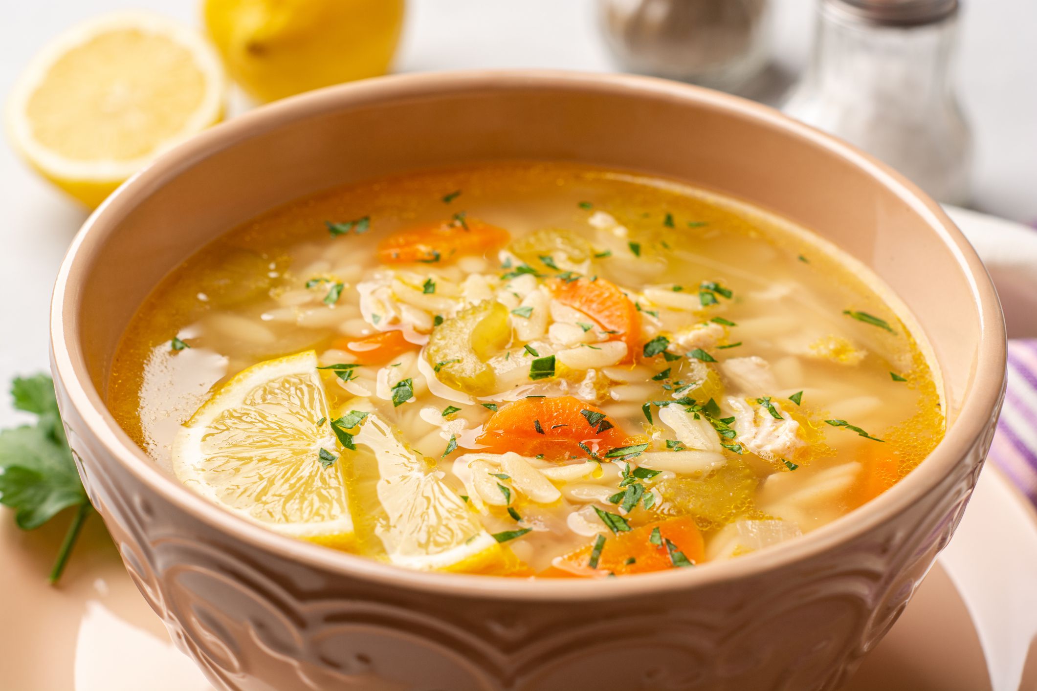 Italian lemon chicken orzo soup in bowl on concrete background. Selective focus.