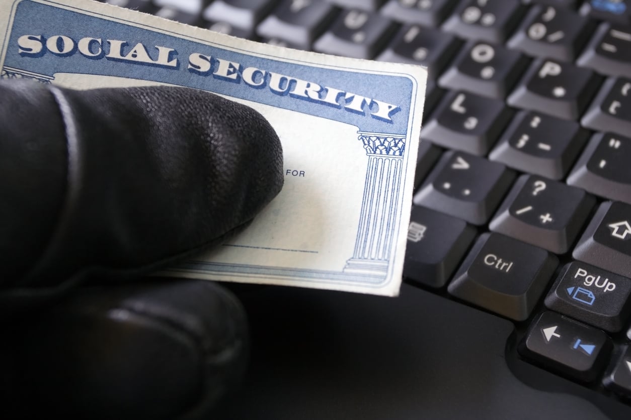 A gloved hand holding a Social Security card over a computer keyboard, suggesting identity theft or cybercrime—and highlighting how AAA member perks can offer identity theft protection.