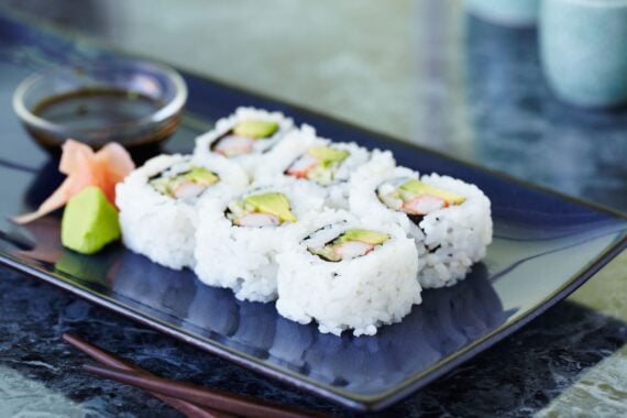 Six California rolls served on a rectangular plate with a side of soy sauce, ginger, and wasabi.