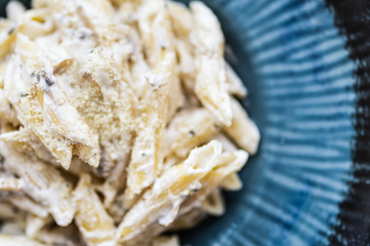 Close-up of creamy penne pasta with a sprinkling of grated cheese on top, served on a blue textured plate.