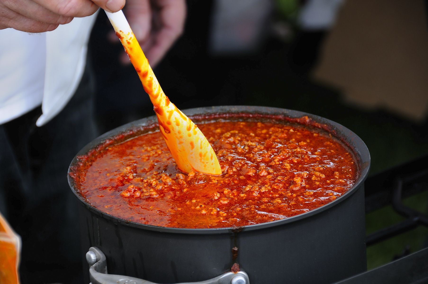 A cook stirs a simmering pot of chili.