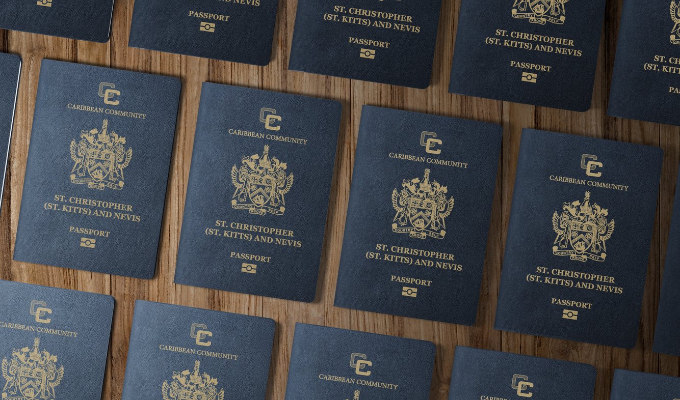 Multiple St. Kitts and Nevis passports with gold lettering and crest are laid out neatly on a wooden surface, showing their covers with the words "Caribbean Community" and "Passport.