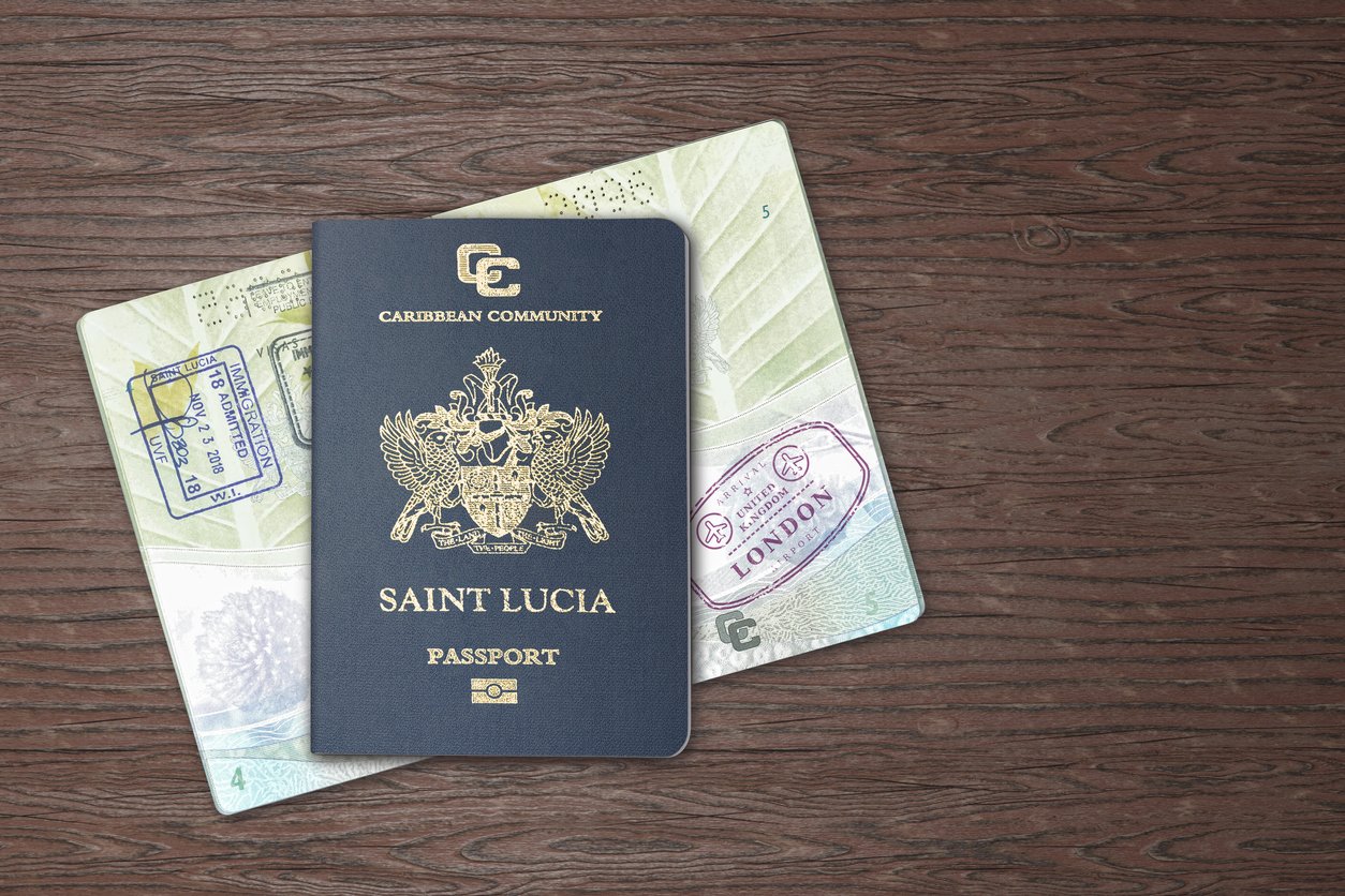 A Saint Lucia passport resting on an open passport displaying visa stamps, including one from London, on a wooden surface.
