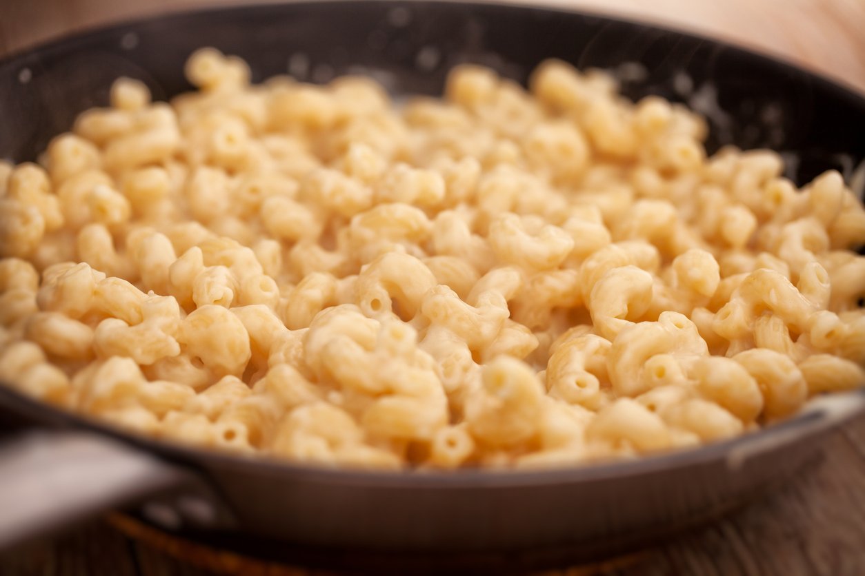 A close-up of creamy macaroni and cheese in a black pan, with soft elbow pasta coated in a smooth cheese sauce.