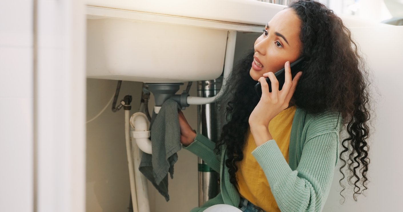 a woman talking on the phone while sitting under a sink
