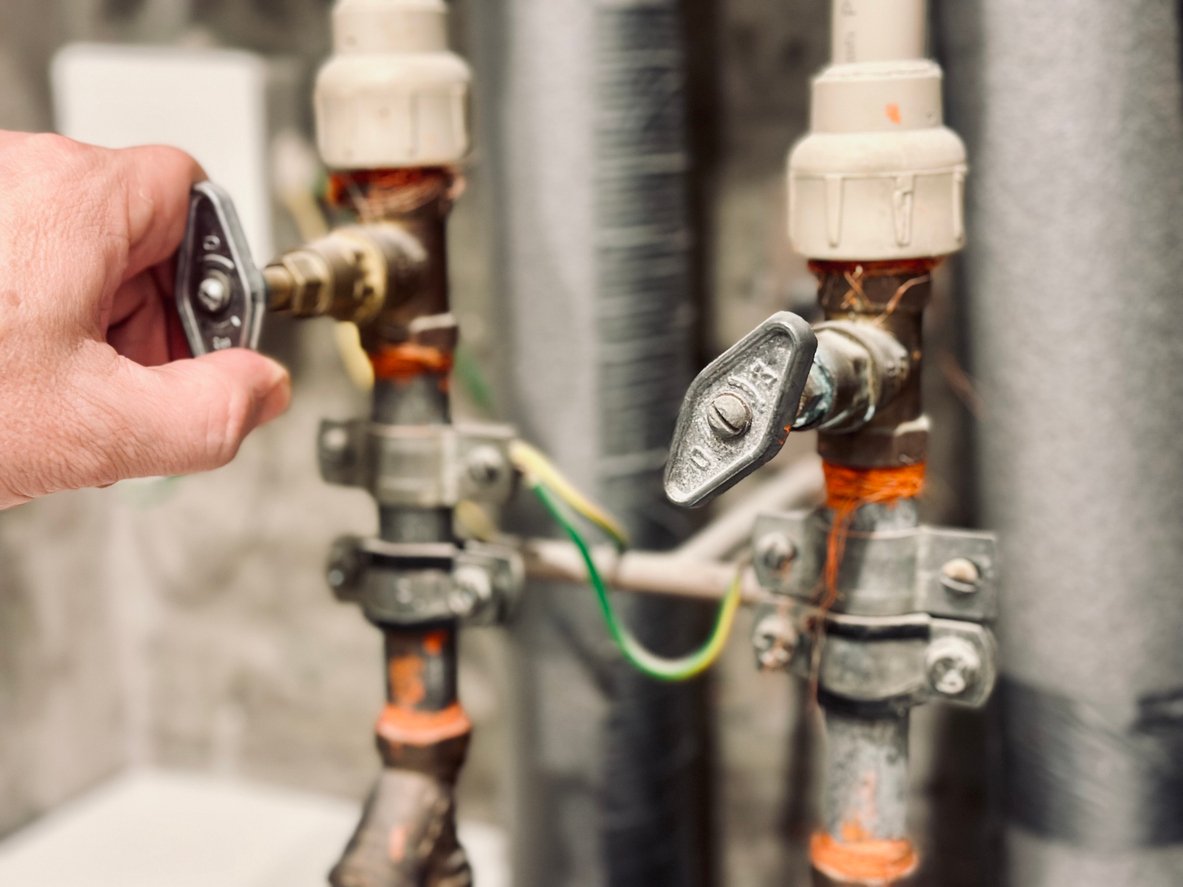 a hand holding a valve to a couple of pipes
