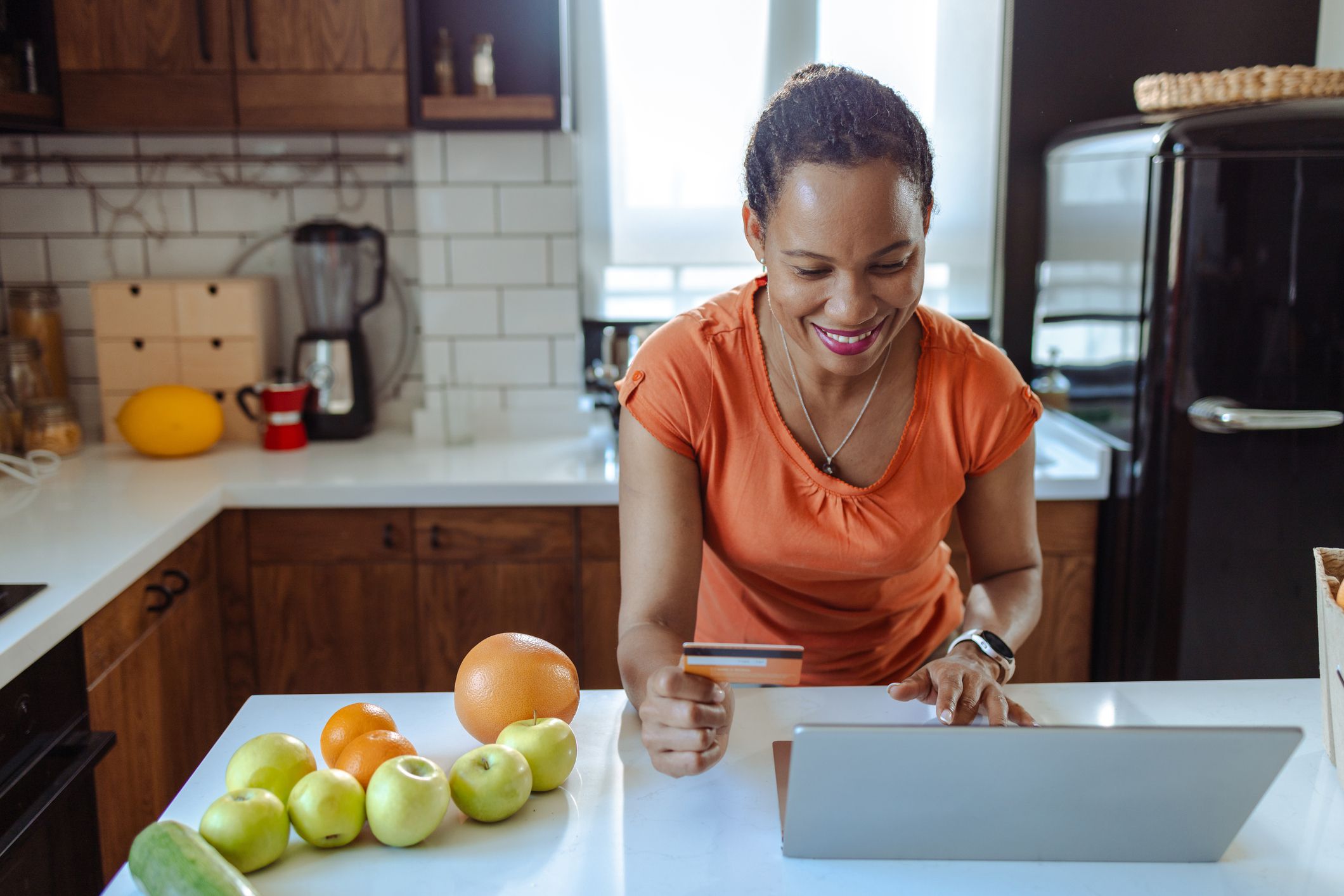 An African American woman just got delivery of fresh organic food. She is using a laptop, a box of organic food is next to her. Online payment with a credit card
