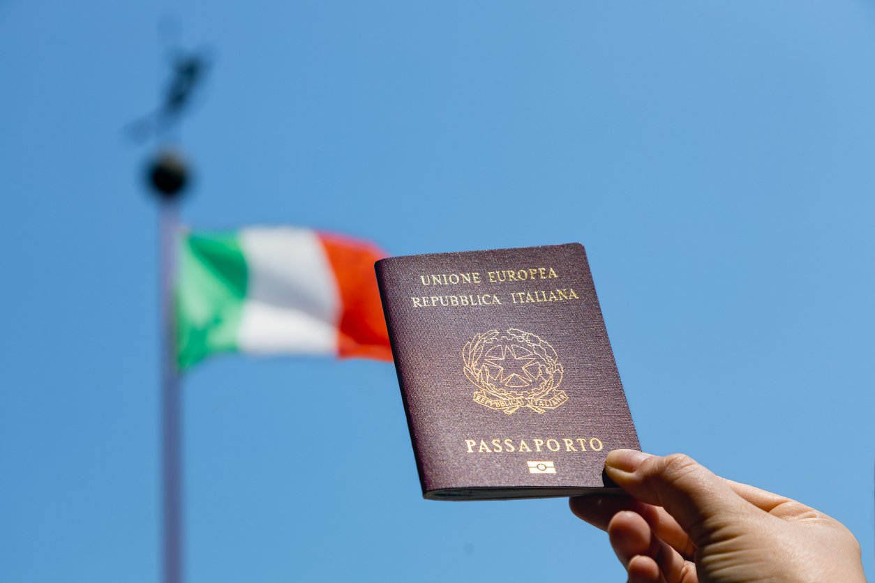 A hand holding a passport in front of a flag