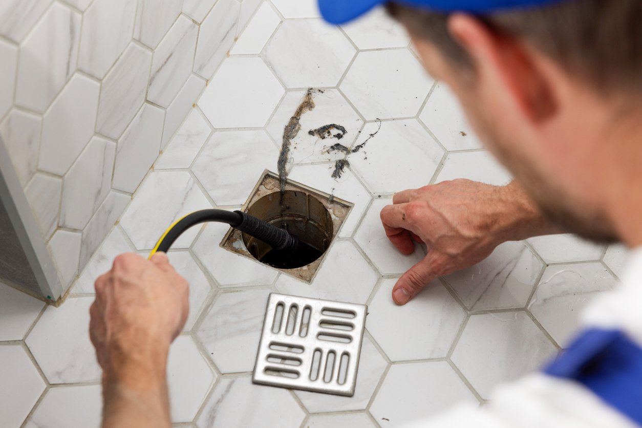 a man using a hose to drain a hole in a tiled floor