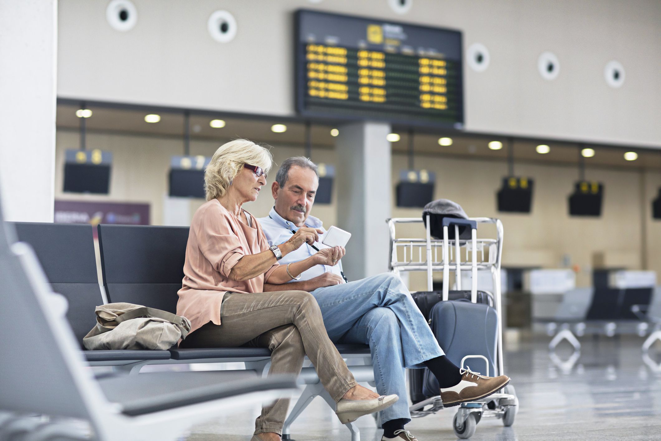 Senior Couple looking at the mobile phone at the airport for information on the new holidays.
