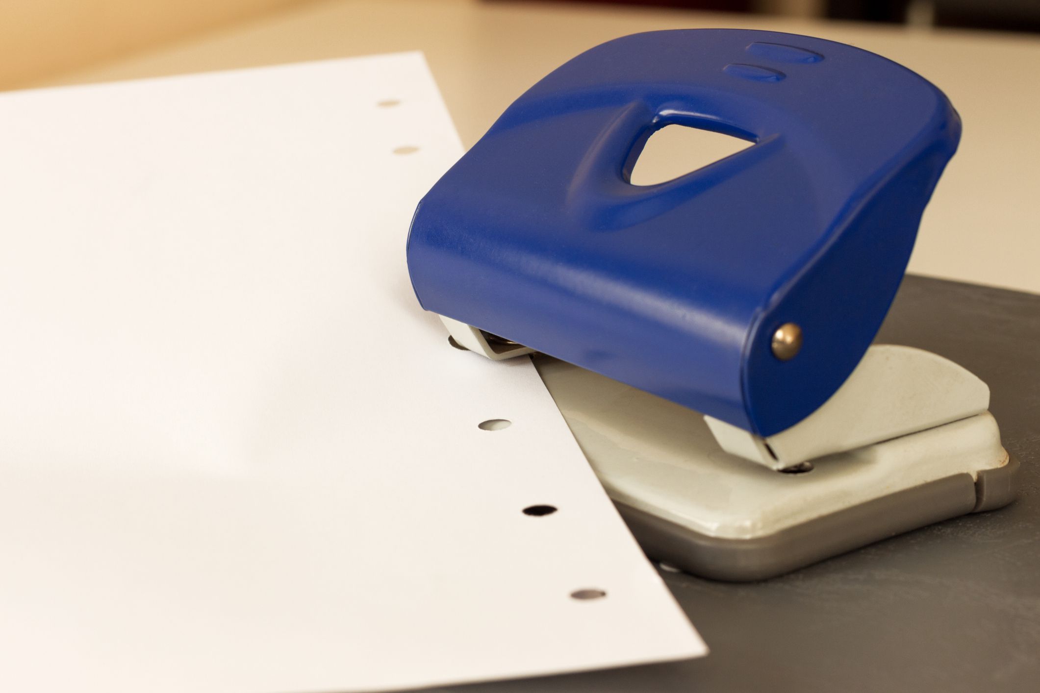 Close up capture of navy blue hole puncher, white paper on grey ground at office