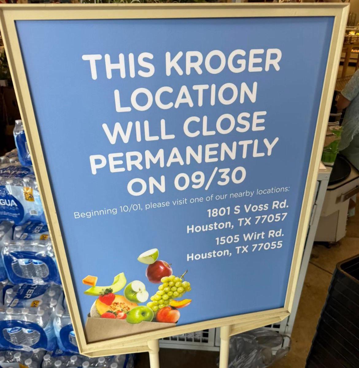 A sign announces that a Kroger location will close permanently on 09/30, listing two nearby Houston addresses. Fruits are pictured at the bottom of the sign; bottled water is visible to the left.
