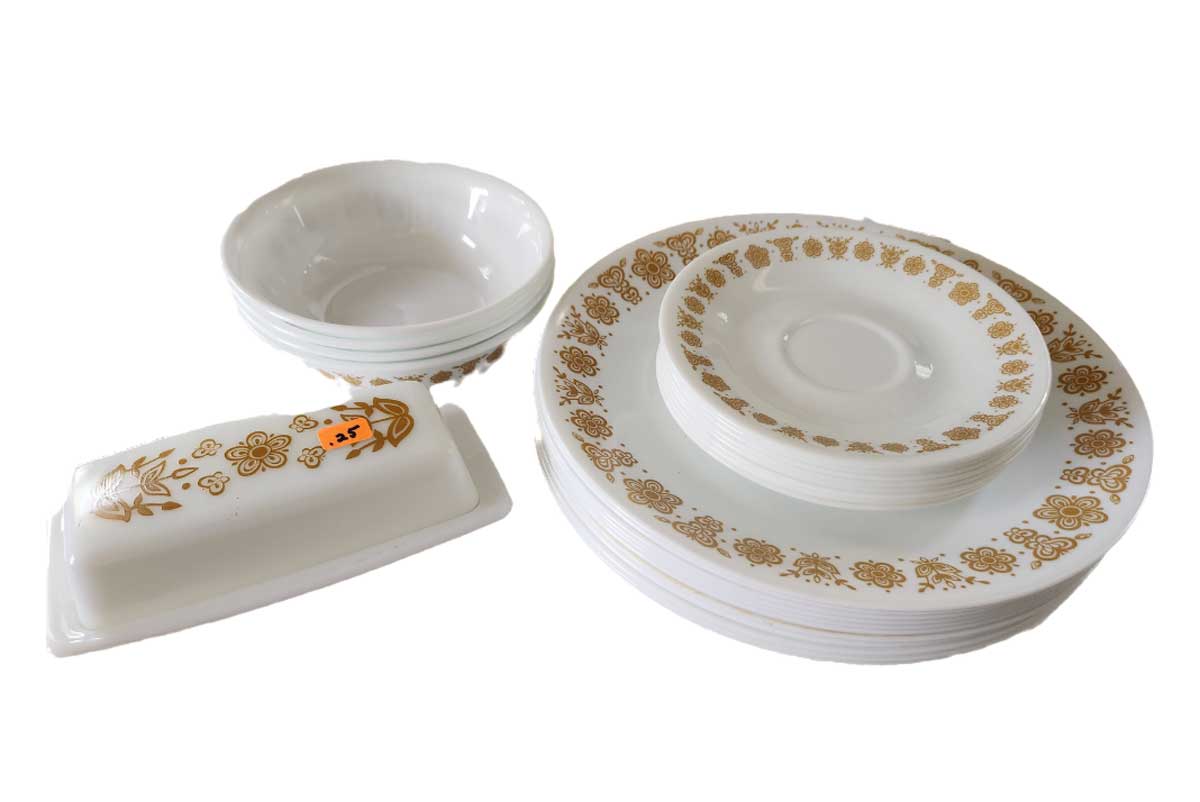 A set of vintage 1980s white dishes with gold floral patterns, including plates, bowls, and a lidded butter dish, all arranged on a white surface. One dish features a small orange price sticker.