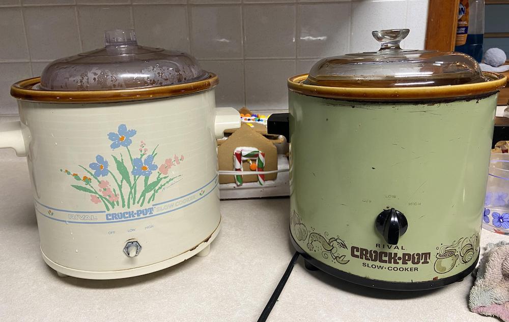 Two vintage Rival Crock-Pot slow cookers sit on a kitchen counter. The left one is cream with a floral design, and the right one is green with decorative patterns. Both have glass lids and brown trim.