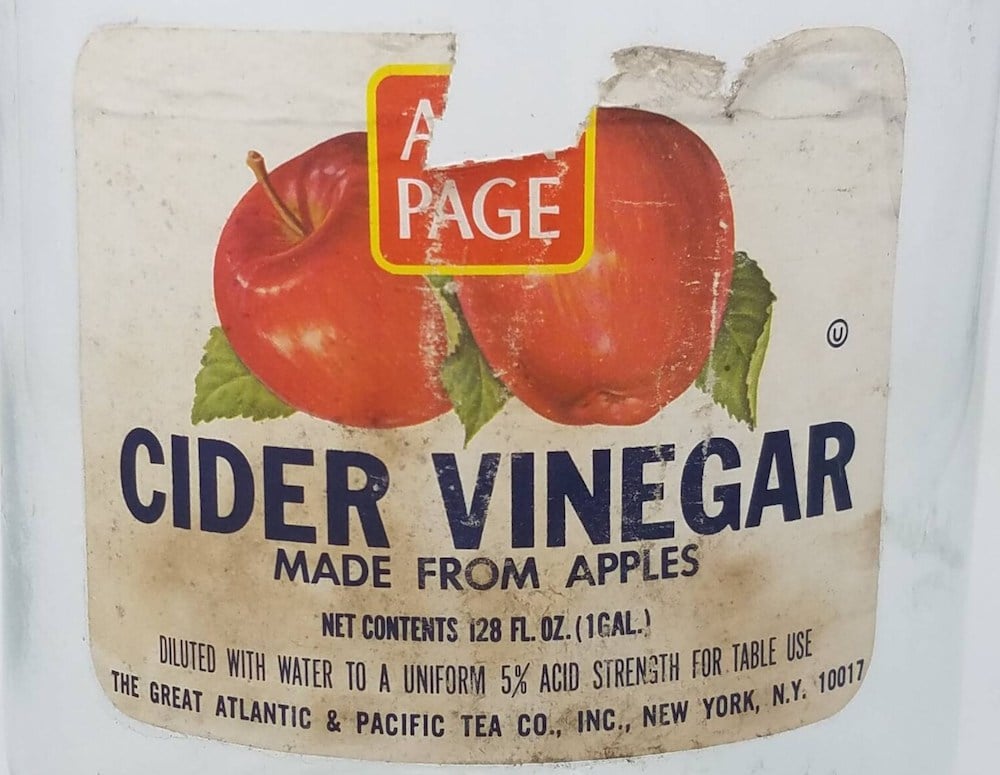 A vintage label for cider vinegar featuring two red apples, the words "Cider Vinegar Made from Apples," and a partially torn "A Page" logo at the top. Text at the bottom lists product details and company information.