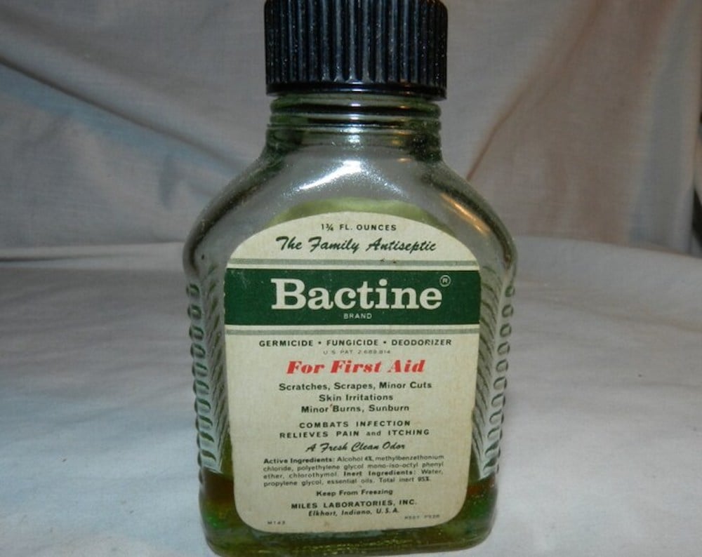 A small, clear glass bottle of Bactine antiseptic with a black cap and a green and cream label detailing its use for first aid, including scratches, scrapes, minor cuts, and burn relief.