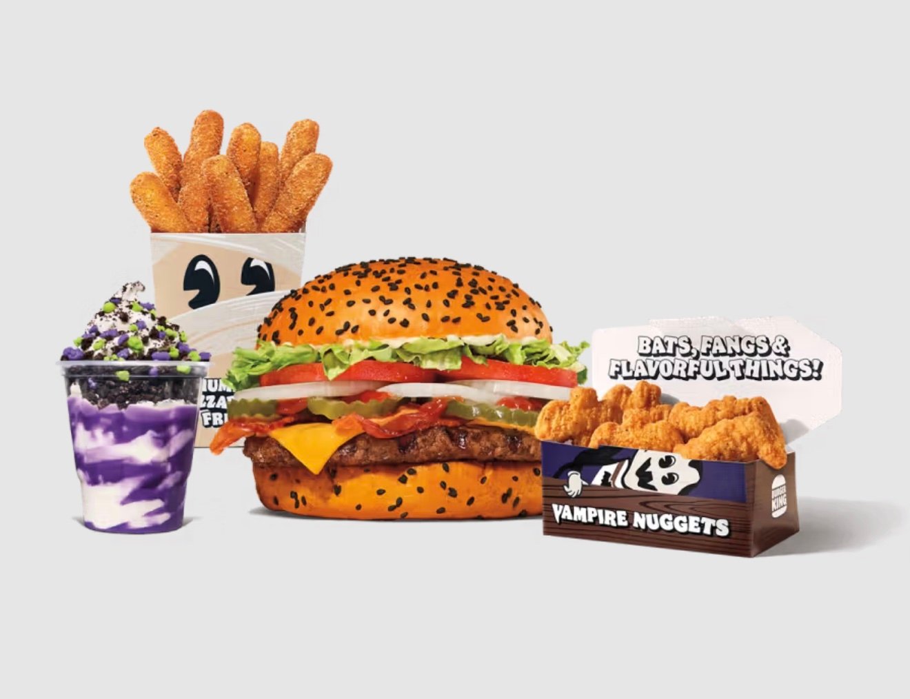 A new fast-food sesame seed bun burger with lettuce, tomato, cheese, and beef patty is surrounded by churros, a purple and white sundae, and a box labeled "Vampire Nuggets" with nugget pieces, all set on a light background.