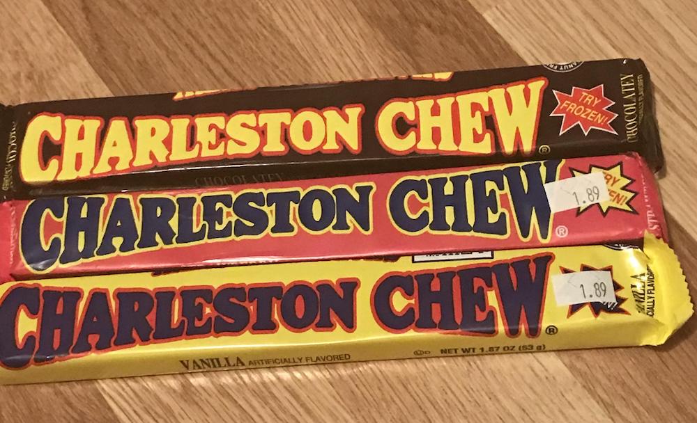 Three Charleston Chew candy bars—chocolate, strawberry, and vanilla flavors—are stacked on a wooden surface. Each bar has a $1.89 price sticker.