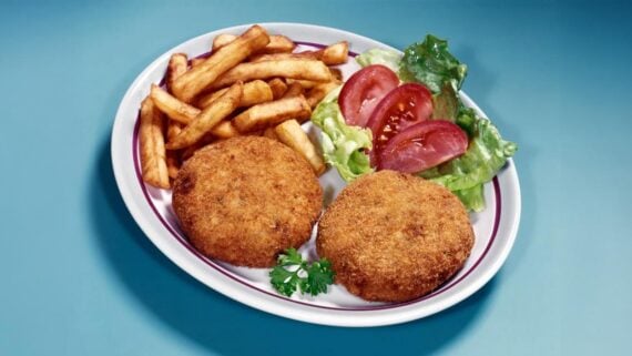 A plate of classic diner foods featuring two breaded crab cakes, crispy French fries, and a small side salad with lettuce and tomato slices, garnished with a sprig of parsley—true to the diners’ tradition of serving the best diner food.