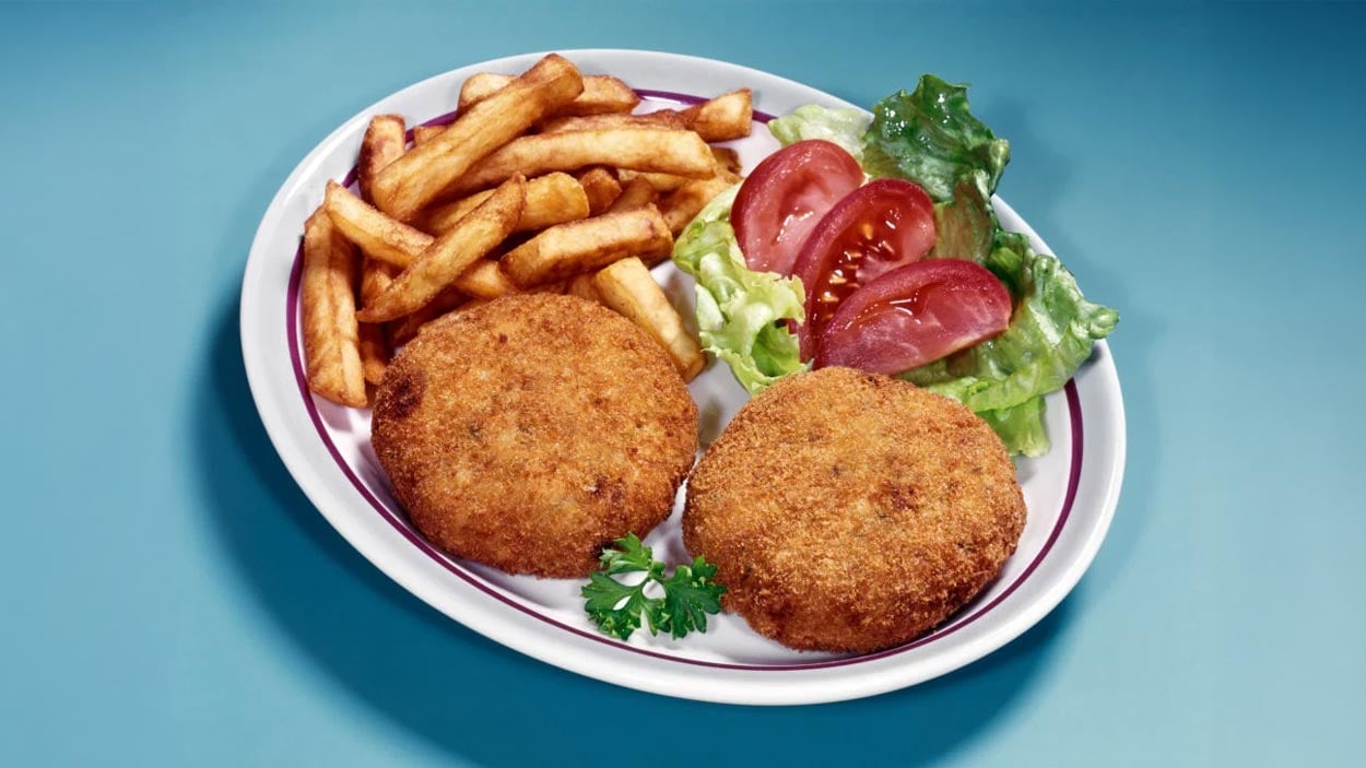 A plate of classic diner foods featuring two breaded crab cakes, crispy French fries, and a small side salad with lettuce and tomato slices, garnished with a sprig of parsley—true to the diners’ tradition of serving the best diner food.