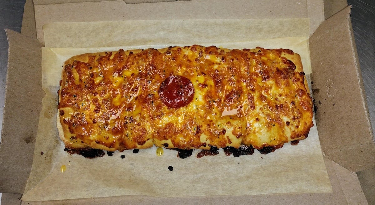 Domino's Stuffed cheesy bread. A rectangular, cheesy bread topped with a single slice of pepperoni in the center, served on parchment paper in a cardboard box.