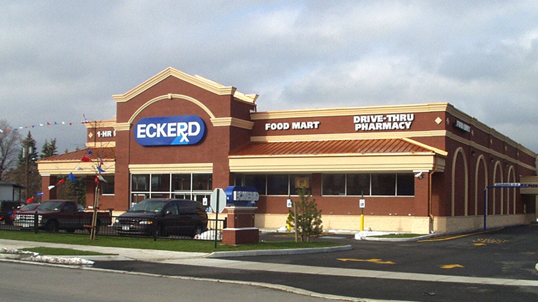 A brick Eckerd store with a drive-thru pharmacy and food mart, featuring a large blue Eckerd sign on the building and cars parked in front, under a cloudy sky.