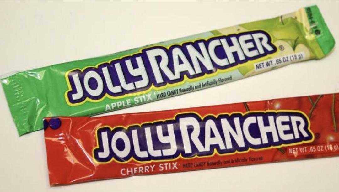 Two Jolly Rancher candy sticks, one in a green apple flavor wrapper and one in a red cherry flavor wrapper, placed on a white surface.
