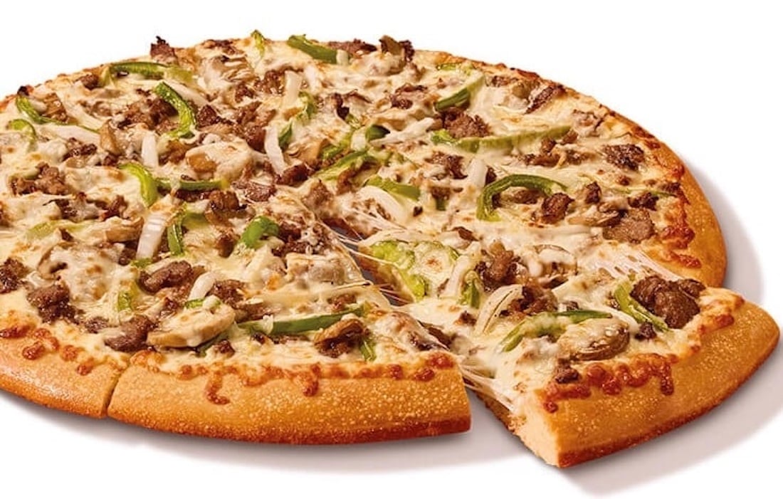 A whole pizza with one slice pulled out, topped with cheese, green bell peppers, onions, and pieces of beef or steak on a golden-brown crust, showcasing a delicious new fast-food favorite against a white background.