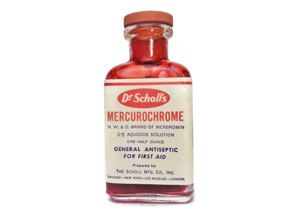 A vintage glass bottle of Dr. Scholl’s Mercurochrome antiseptic, containing a red liquid and labeled for general first aid use, with dosage details and manufacturer information on the front.