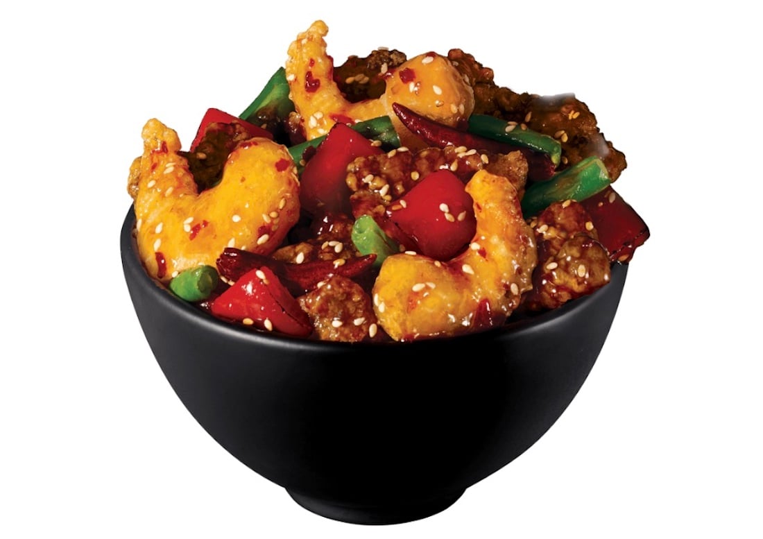 A black bowl filled with crispy shrimp, red bell peppers, green beans, and sesame seeds, all coated in a glossy, spicy-looking sauce—a vibrant new fast-food option. The background is plain white.