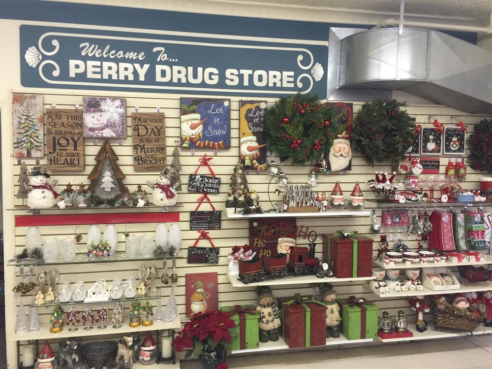 A store display at Perry Drug Store features festive holiday decorations, including wreaths, Santa figurines, holiday signs, snowmen, nutcrackers, gift boxes, and poinsettias arranged on shelves and hanging on the wall.