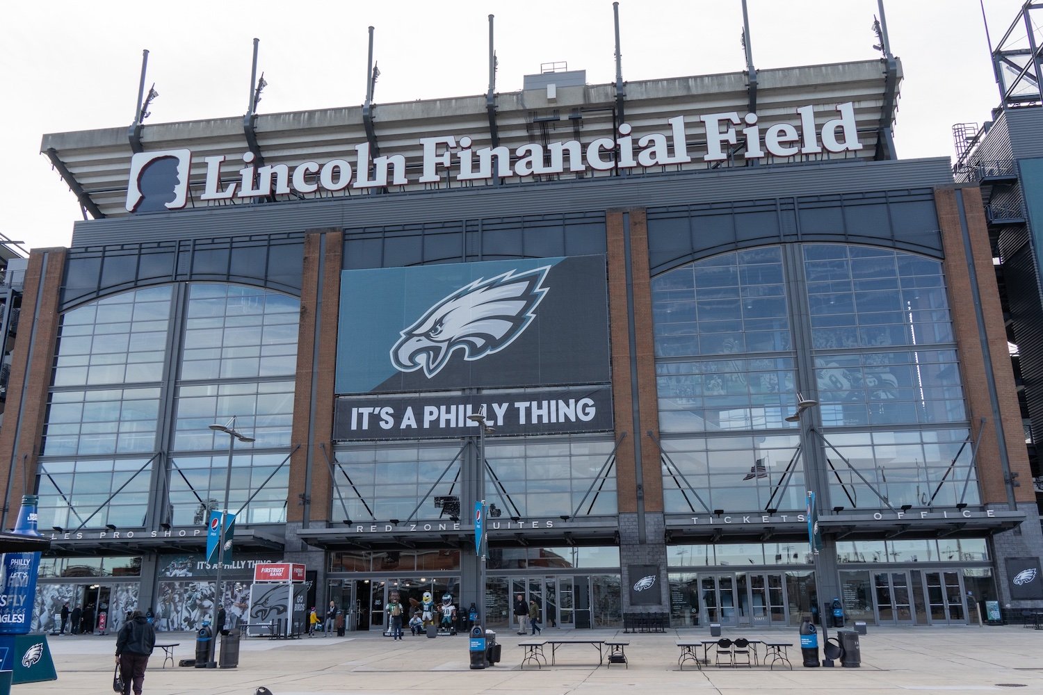 The front entrance of Lincoln Financial Field, with large glass windows, the Philadelphia Eagles logo, and a sign reading "IT'S A PHILLY THING" displayed above the doors.