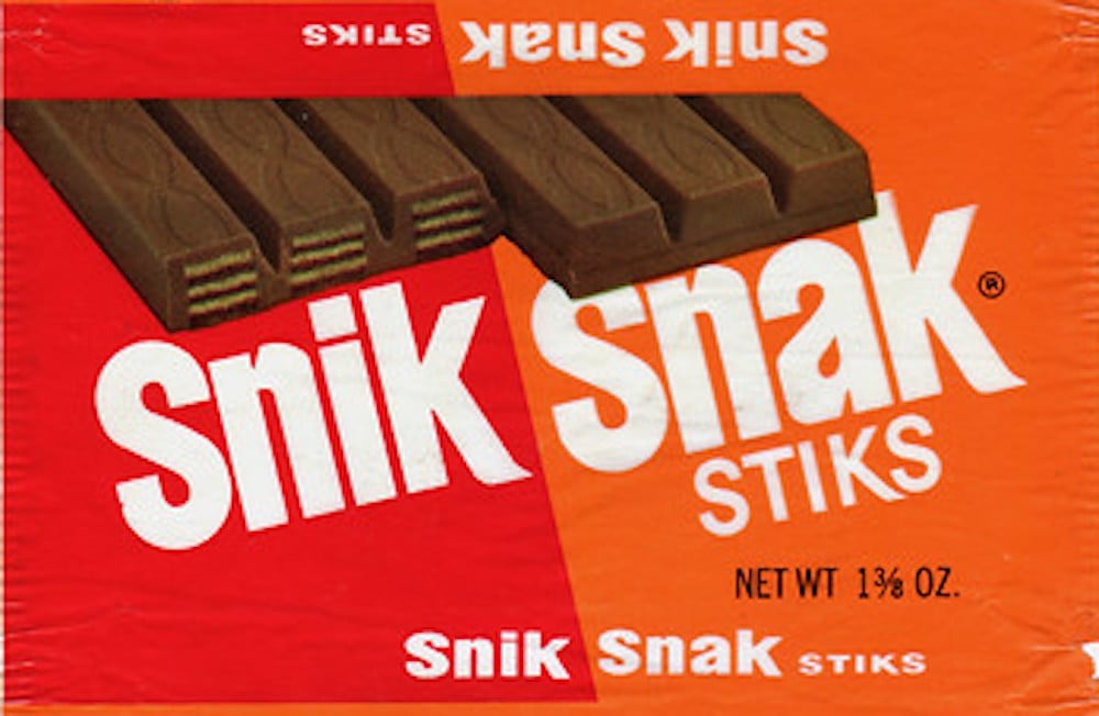Vintage candy wrapper for "Snik Snak Stiks," showing chocolate-covered wafer bars and bold white text on a red-orange background. The net weight is 1⅜ oz.