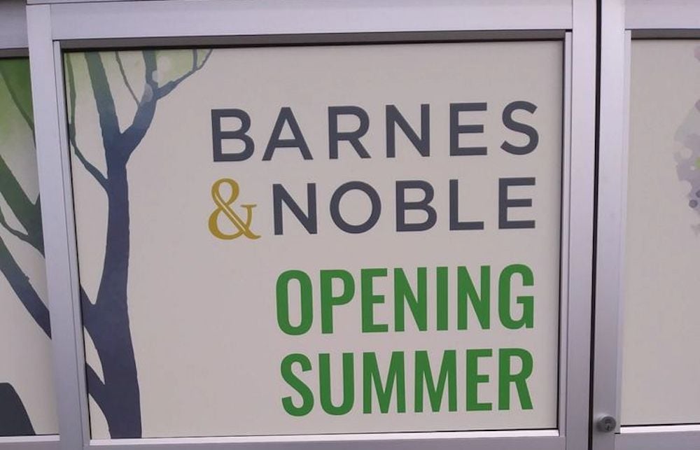 A sign on a storefront window reads "Barnes & Noble Opening Summer" in large letters, with tree illustrations in the background.