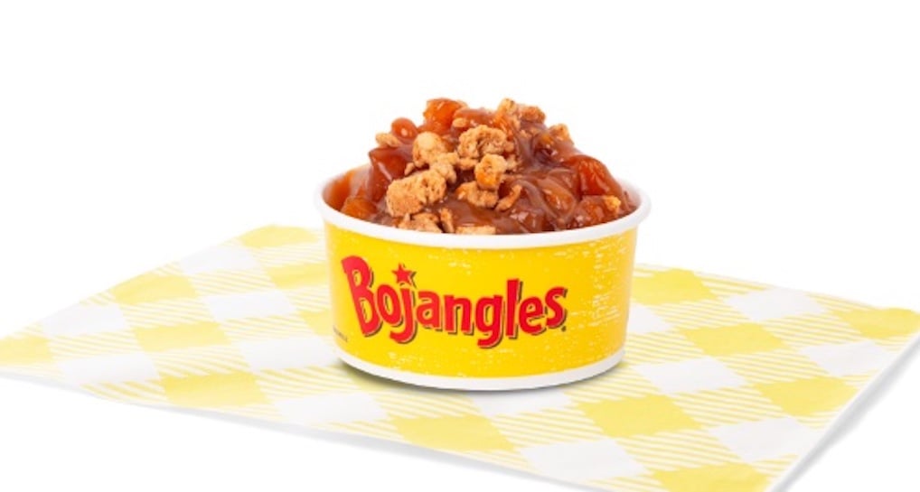 A Bojangles branded cup filled with gravy and crumbled sausage pieces, inspired by new fast-food trends, sits on a yellow and white checkered napkin against a white background.
