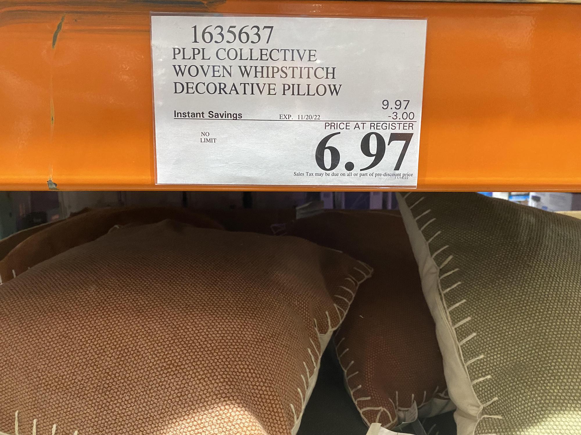 Decorative pillows with whipstitch edges in orange and green colors are displayed on a shelf below a price tag showing an instant savings offer, with the final price listed as $6.97 at Costco.