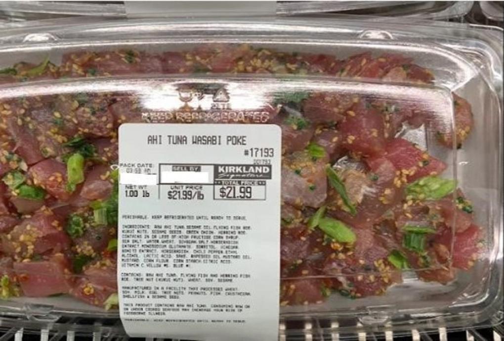 A plastic container of Kirkland Signature Ahi Tuna Wasabi Poke, showing diced raw tuna mixed with green onions and seasonings. The price label displays $21.99 per pound and the weight as 1.01 lbs.
