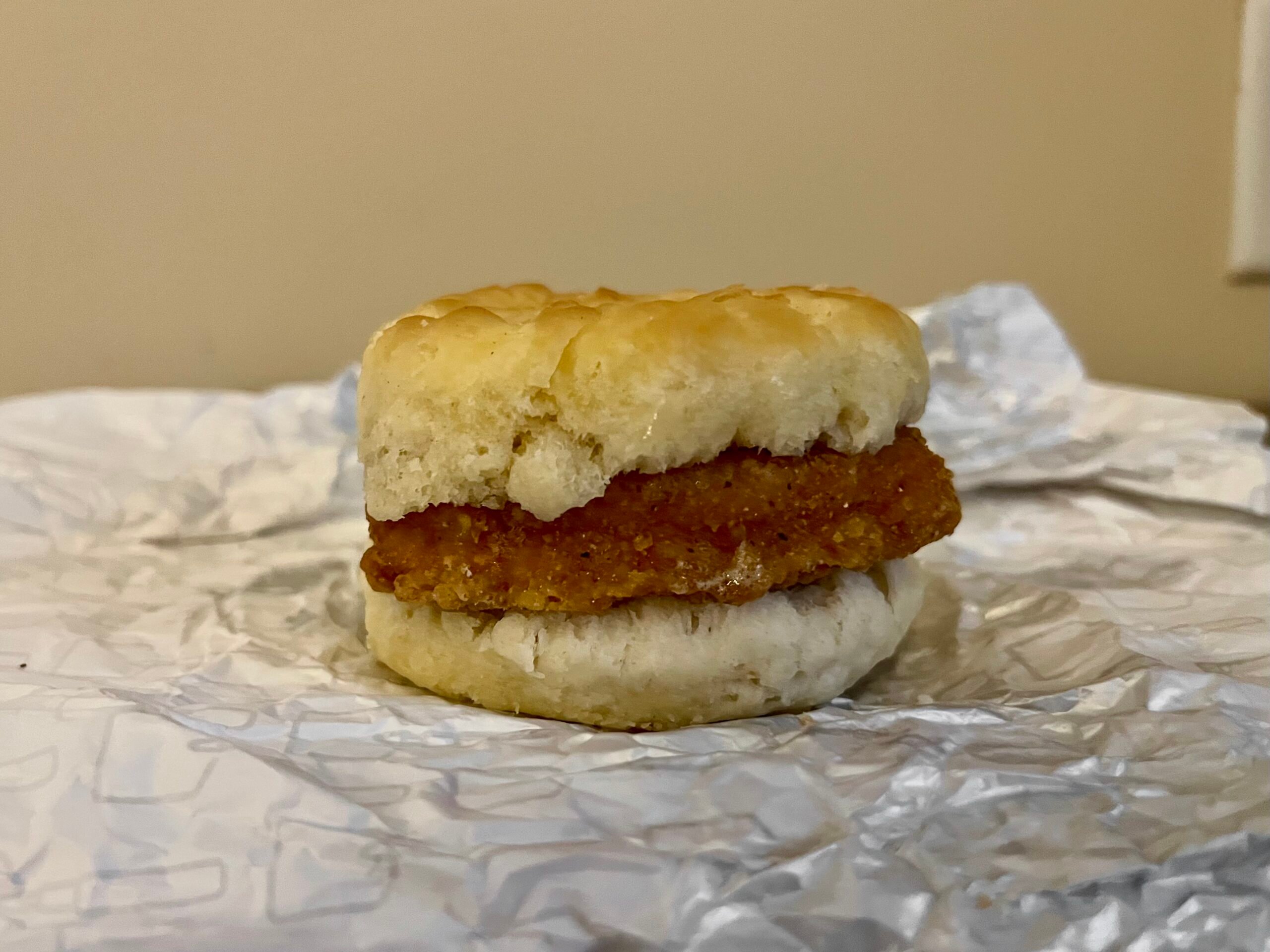 A crispy chicken patty is sandwiched between two halves of a biscuit, sitting on crumpled white paper with a beige wall in the background. Ranked at the top of Wendy's breakfast menu in our taste test.
