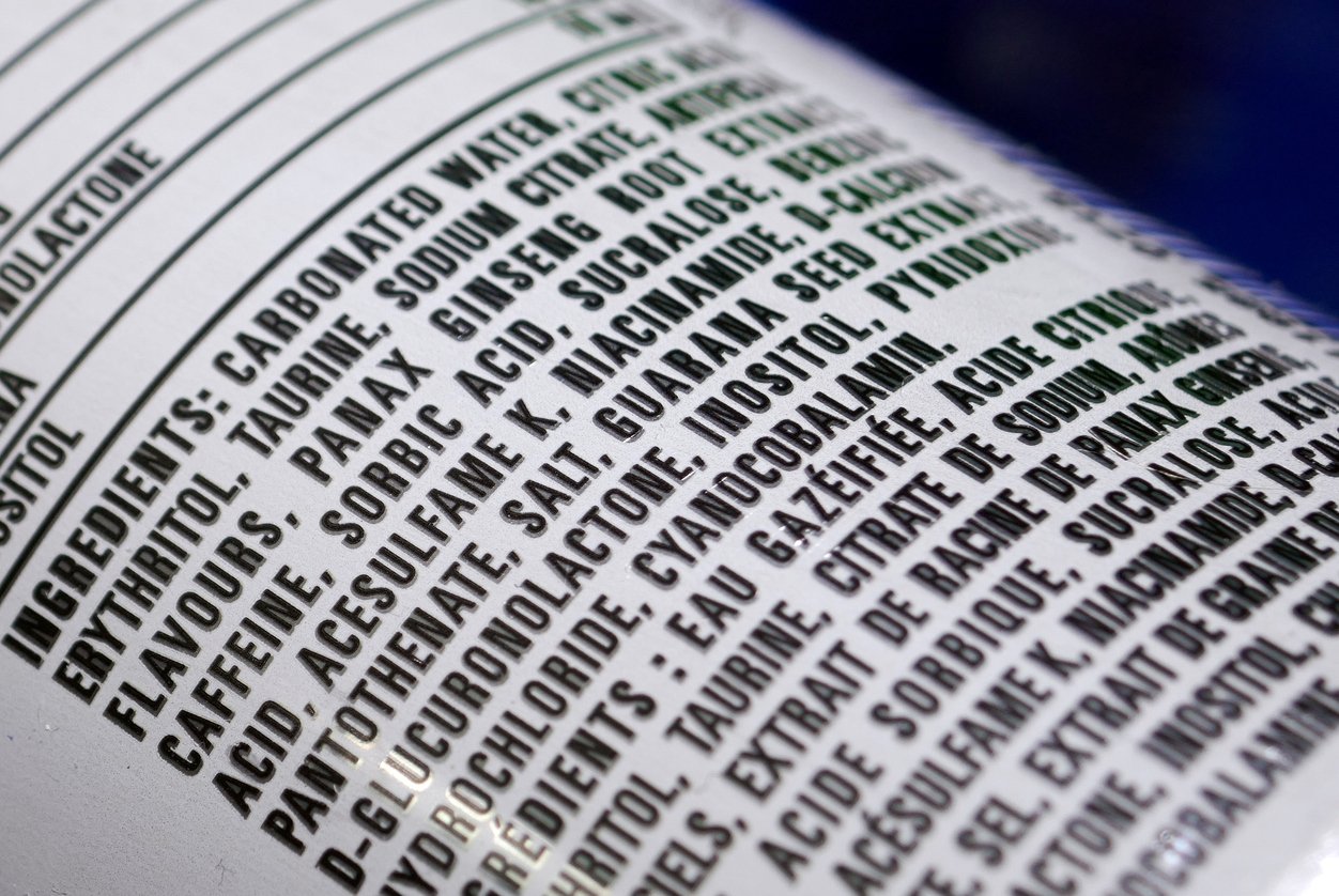 Close-up of a product label listing ingredients such as carbonated water, citric acid, flavors, caffeine, Panax ginseng, sucralose, acesulfame K, sodium citrate, and guarana seed extract in bold black text.