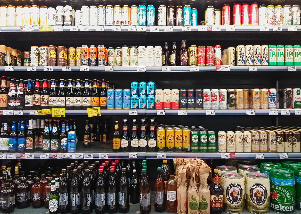Shelves in a store display a wide variety of canned and bottled beers, arranged by type and brand, with colorful labels and packaging in multiple rows.