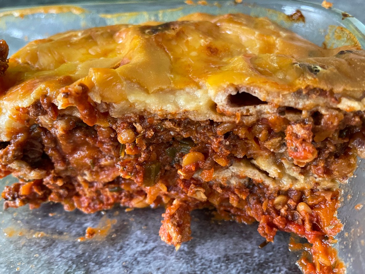 A close-up of a sliced lasagna in a glass baking dish, showing layers of pasta, meat sauce, and melted cheese, with a rich, juicy texture and slightly browned cheese on top.