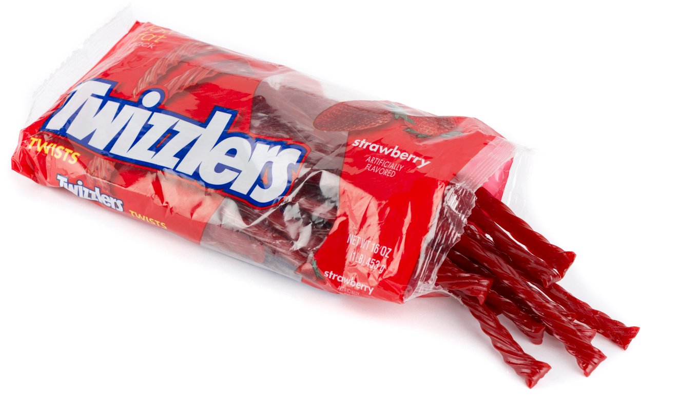 An open package of Twizzlers strawberry-flavored candy with several red twisted licorice sticks partially pulled out of the bag, lying on a white surface.