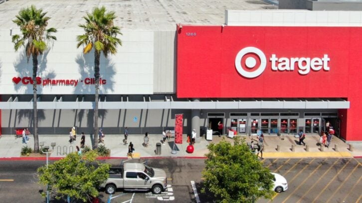 Aerial view of a Target store with a CVS pharmacy inside. People are walking in and out of the entrance, with several palm trees and parked vehicles visible in front of the building.