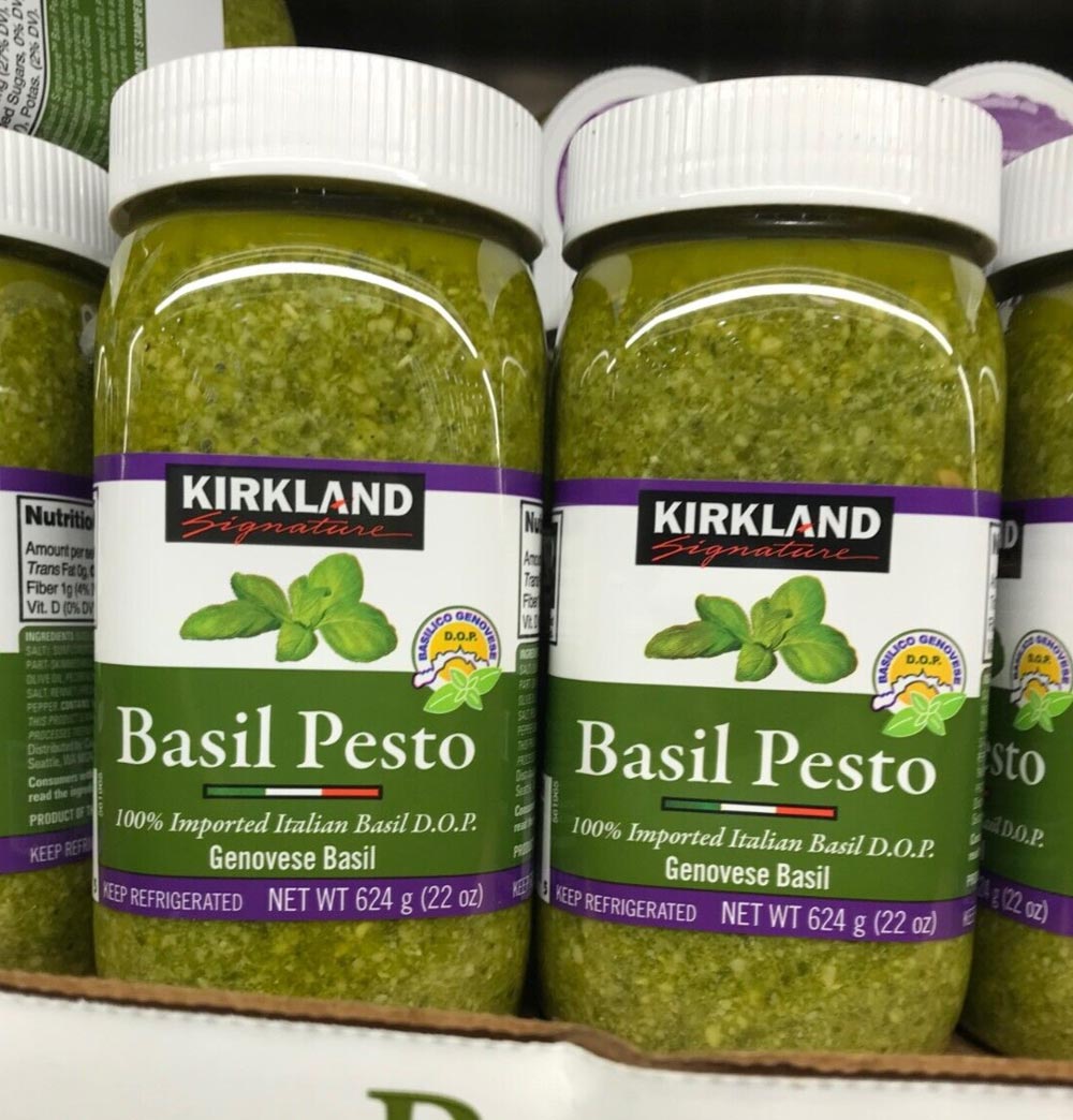 Close-up of jars of Kirkland Signature Basil Pesto, a Costco product loved by shoppers. The green pesto is visible through clear jars labeled “100% Imported Italian Basil D.O.P. Genovese Basil, NET WT 624g (22oz).”