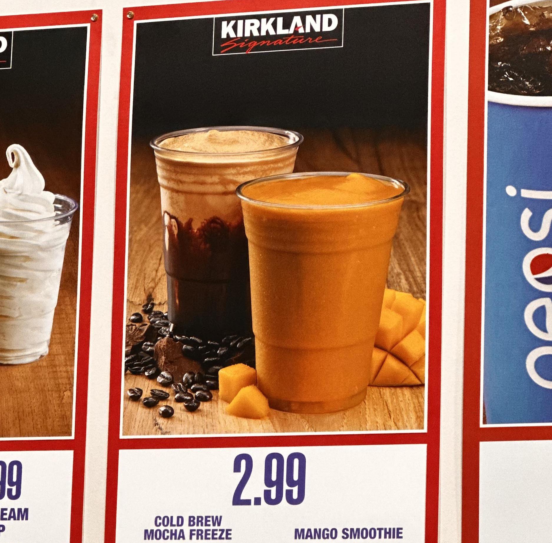 Two plastic cups filled with cold beverages are on display; one is a cold brew mocha freeze with coffee beans and chocolate, and the other is a bright orange mango smoothie with mango chunks beside it. Price: $2.99. Costco Kirkland Food Court Menu