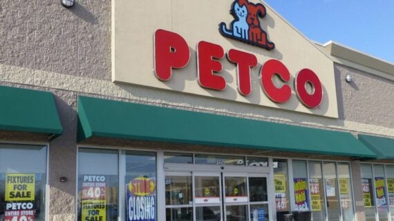 The exterior of a Petco store with large red letters and a pet logo above the entrance. Storefront windows display multiple "Store Closing" and "For Sale" signs.